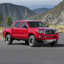 Load image into Gallery viewer, The red Old Man Emu Toyota Tacoma with its impressive ground clearance is parked in front of mountains.