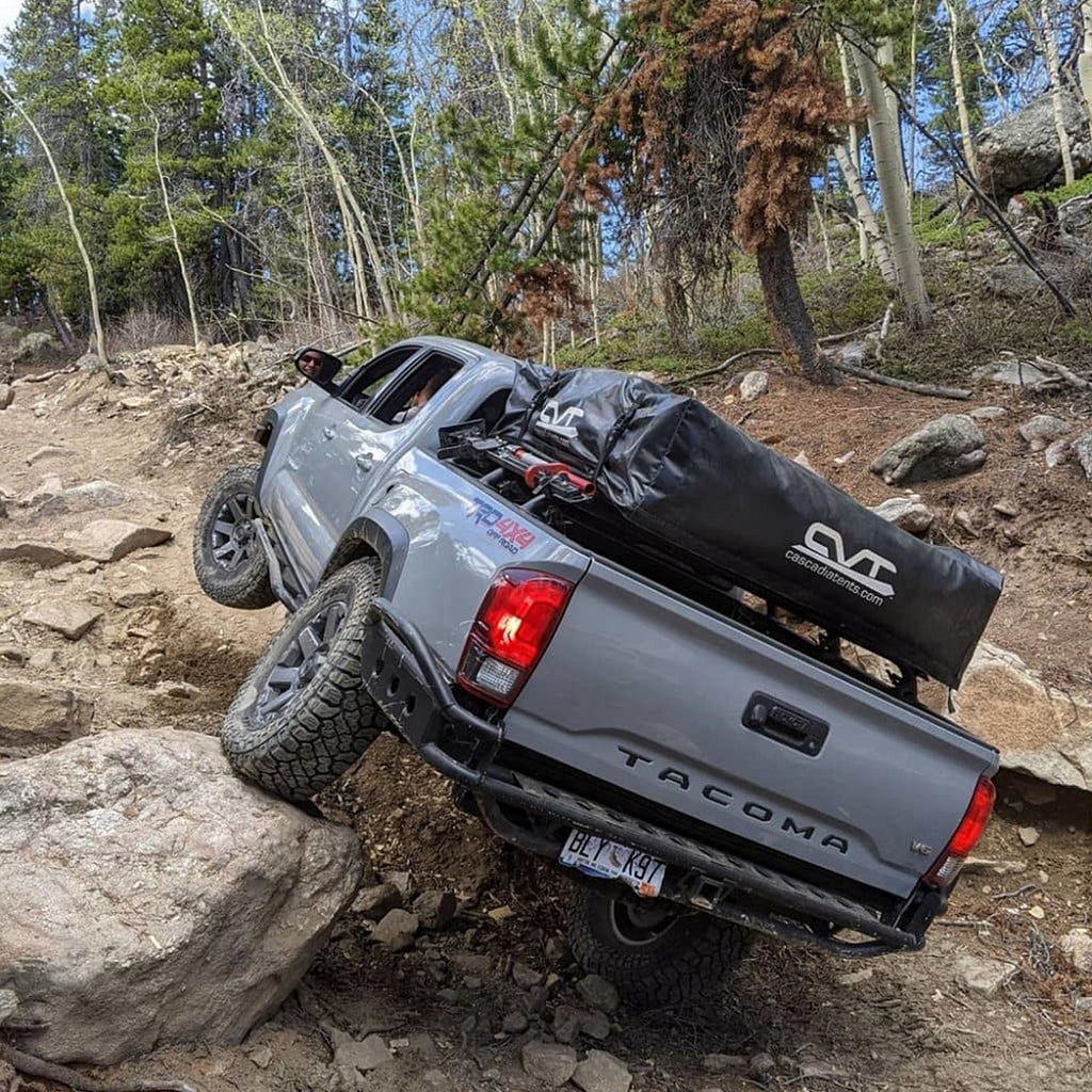 A Toyota Tacoma equipped with the Old Man Emu 2 inch Essentials Lift Kit for Tacoma (16-23) is confidently driving down a rocky trail, showcasing its exceptional suspension system.