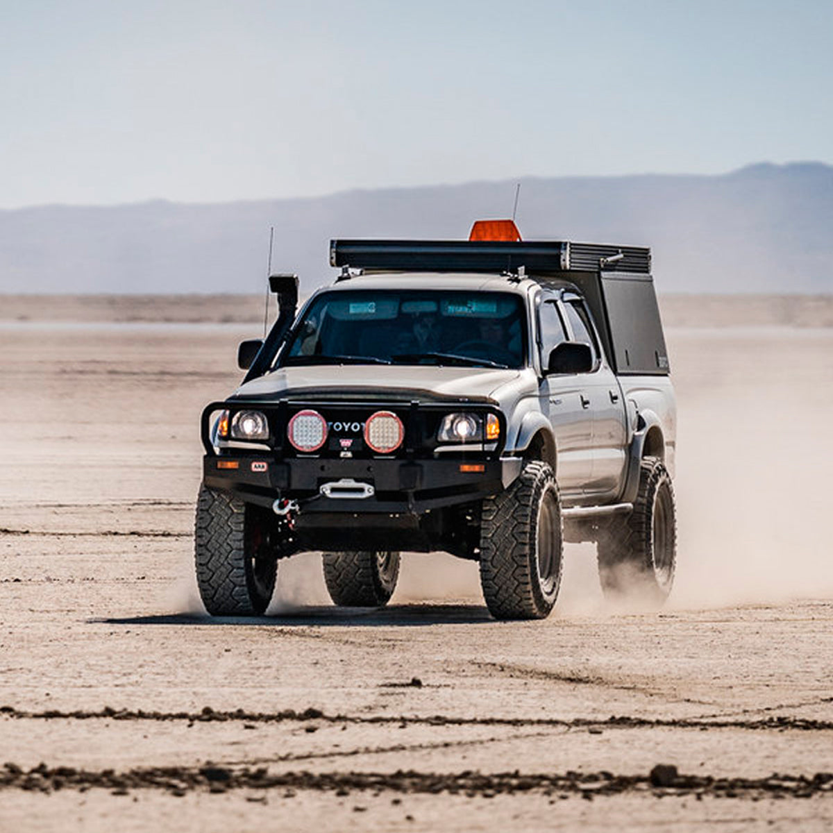 An Old Man Emu 2 inch Lift Kit for Tacoma (98-04) pickup truck with an increased ground clearance driving through the desert.