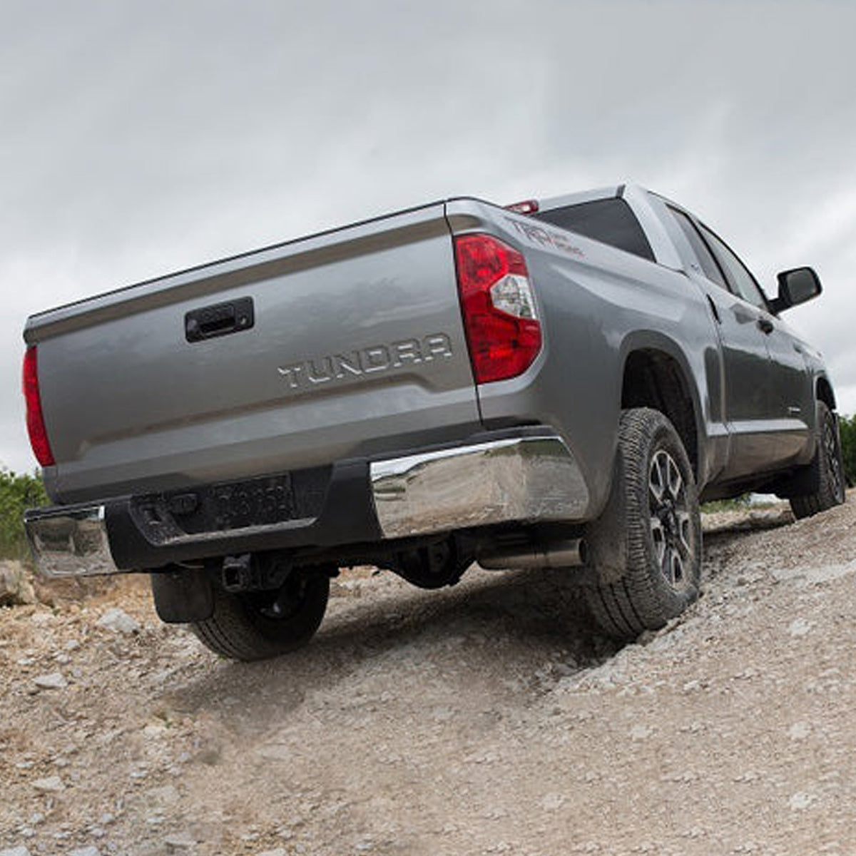 The rear end of a gray Toyota Tundra equipped with an Old Man Emu 2.5 inch Lift Kit for Tundra (07-21) suspension system and Nitrocharger shocks, traversing a dirt road.