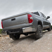 Load image into Gallery viewer, The rear end of a gray Toyota Tundra on a dirt road, showcasing its increased ground clearance thanks to the Old Man Emu 2.5 inch Essentials Lift Kit for Tundra (07-21) suspension system and Nitrocharger shocks.