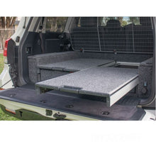 Load image into Gallery viewer, The back of a SUV with an ARB Outback Solutions Mid-Height Roller Floor RFH945 featuring an anti-rattle design for maximum security and being dust and water resistant.