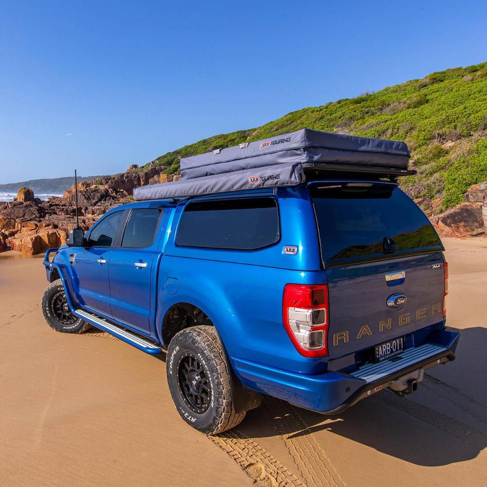 Blue 2020 Ford Ranger with ARB Flinders Rooftop Tent 803300A mounted, rugged off-road tires, and canopy on sandy beach terrain.