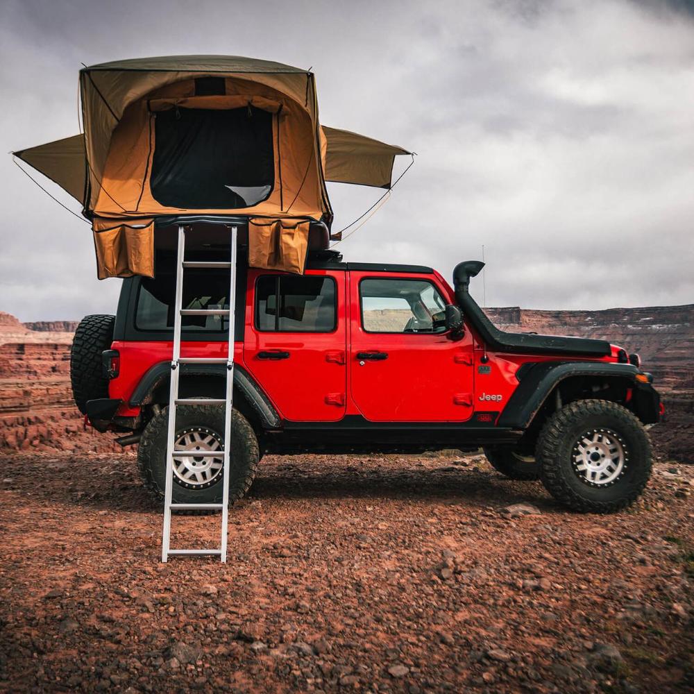 ARB Flinders Rooftop Tent 803300A mounted on red 2002-2013 Jeep Cherokee Liberty KJ with ladder extended in desert terrain
