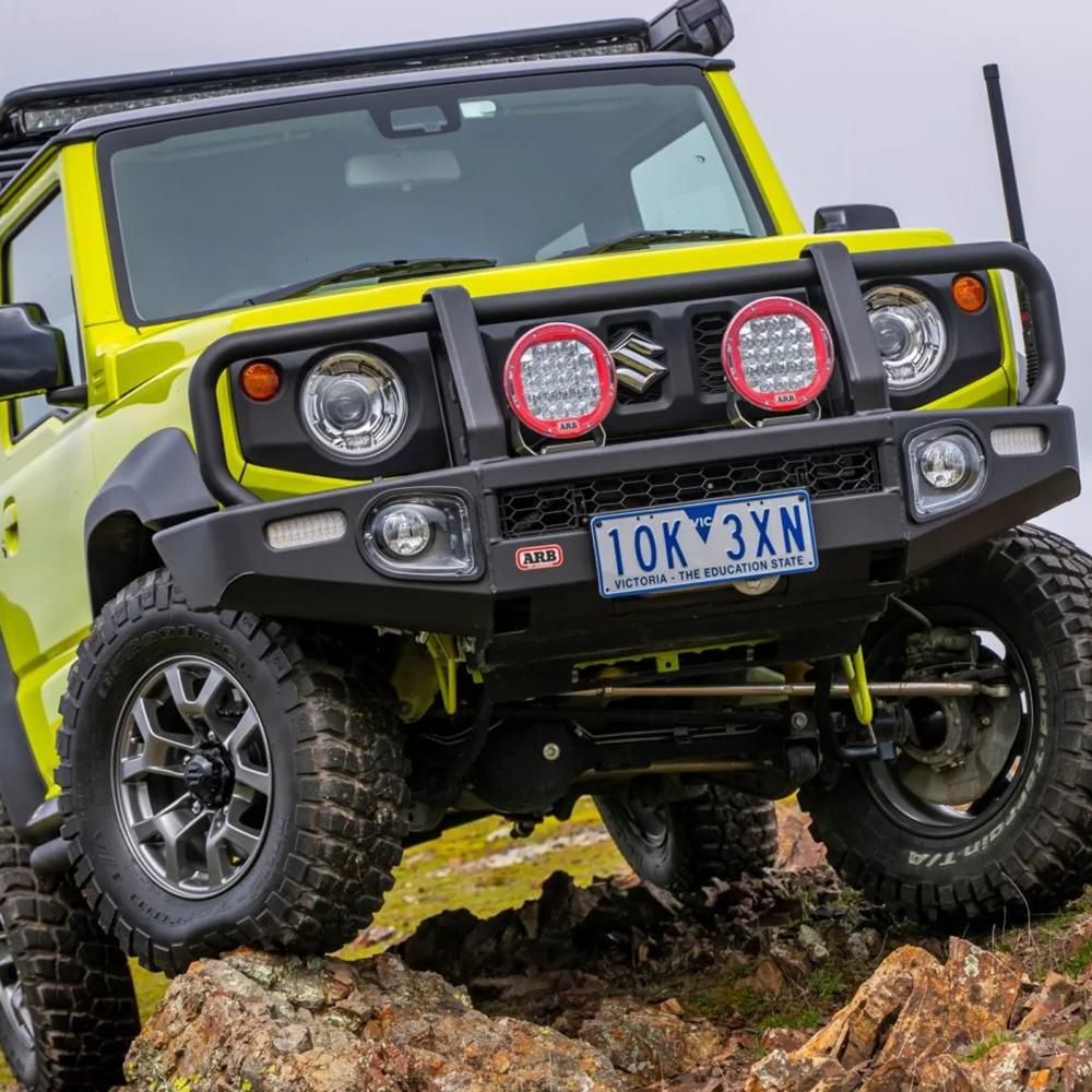 A yellow jeep equipped with an ARB Old Man Emu Front Nitrocharger Sport 60154 for Suzuki Jimny (4th Gen) 4 Cylinder 1.5L Petrol Engine All Models is driving on a rocky hill.