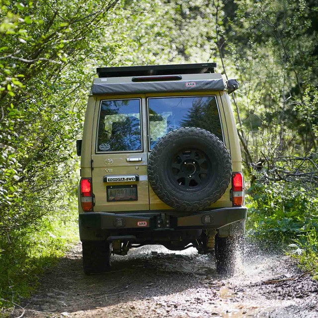 ARB Touring Awning 814301 (49.21” x 82.67”) mounted on rugged Toyota 4WD, deployed for shade during forest trail off-road driving