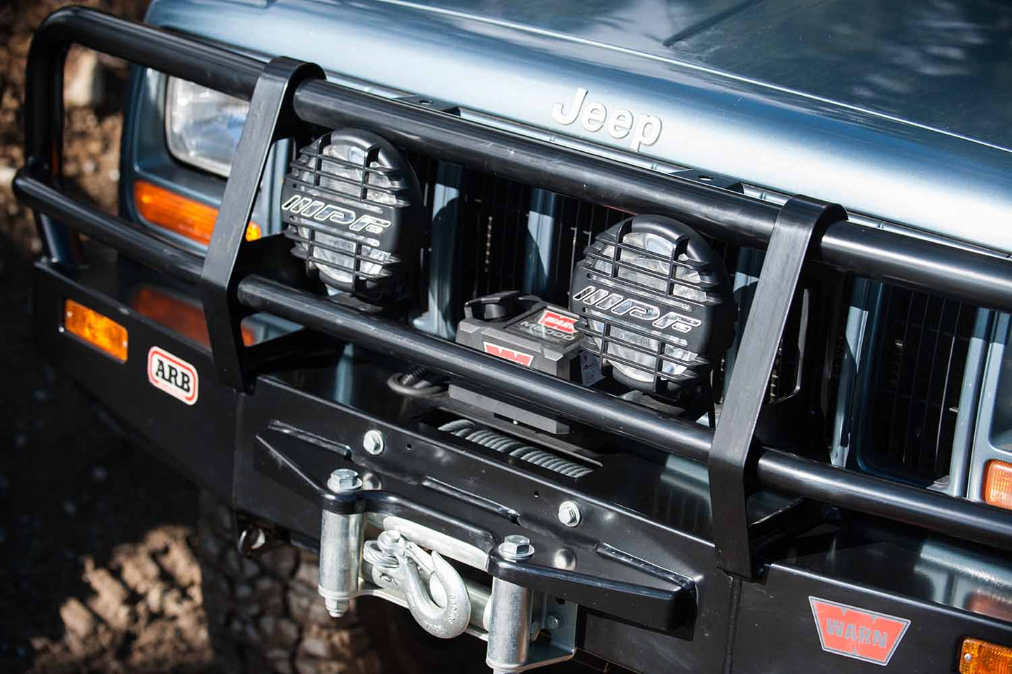 ARB IPF Driving Light Kit 968CSG with high-impact black resin body, polished glass lens, and adjustable mounting on Jeep Cherokee front bumper