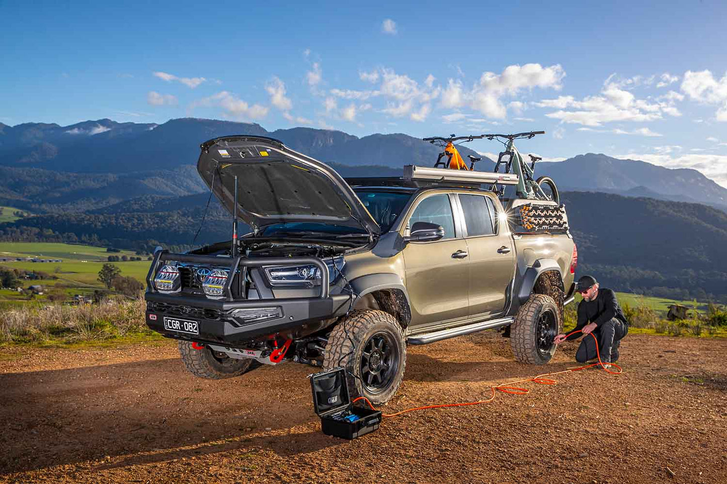ARB Portable 12V Air Compressor Single Motor CKMP12V2 inflating tire on lifted off-road truck in mountain terrain with accessories