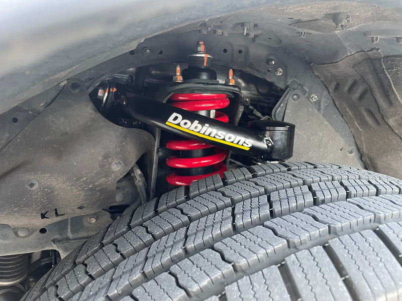 Dobinsons heavy-duty suspension coil spring and control arm above a truck tireлириниң
