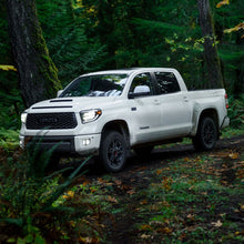 Load image into Gallery viewer, The Old Man Emu BP-51 Fit Kit Front VM80010034 for Toyota Tundra 2007 - 2021 is driving through the woods, showcasing its exceptional suspension system for a smooth ride quality.