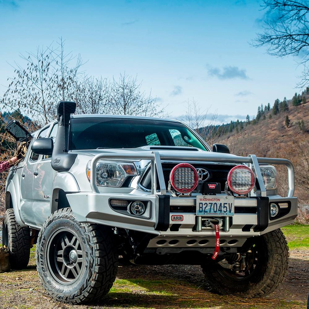 An Old Man Emu Toyota Tacoma with ARB Old Man Emu Front Coil Springs 2886 implementing an easy installation is parked next to a tree.