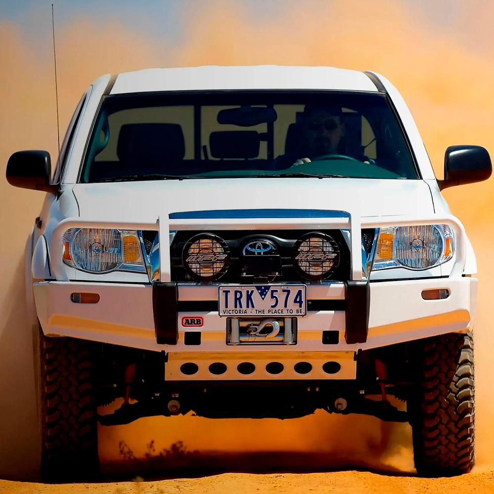 A white truck driving through sand in the desert, equipped with the Old Man Emu ARB Front Nitrocharger Sport Strut 90010 for Toyota 4Runner/ FJ Cruiser / Prado 150 Series heavy gauge reserve tube and high-quality oil.