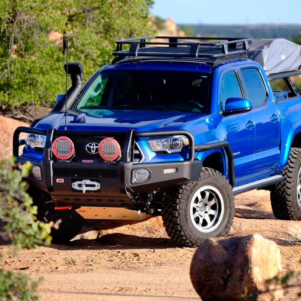 A blue Toyota Tacoma, equipped with the ARB Old Man Emu Driveshaft Spacer Kit, is parked in the desert.