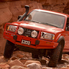 Load image into Gallery viewer, An Old Man Emu red pickup truck driving through a rocky area with progressively distributed bumps.