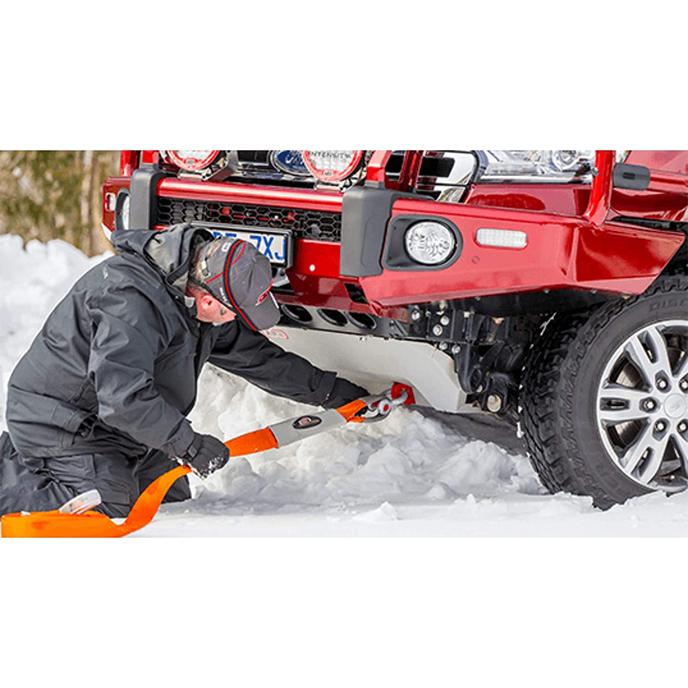 A man using an ARB Weekender Recovery Kit RK12A to clear snow from a truck with a PVC outer shell.
