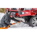A man using an ARB Weekender Recovery Kit RK12A to clear snow from a truck with a PVC outer shell.