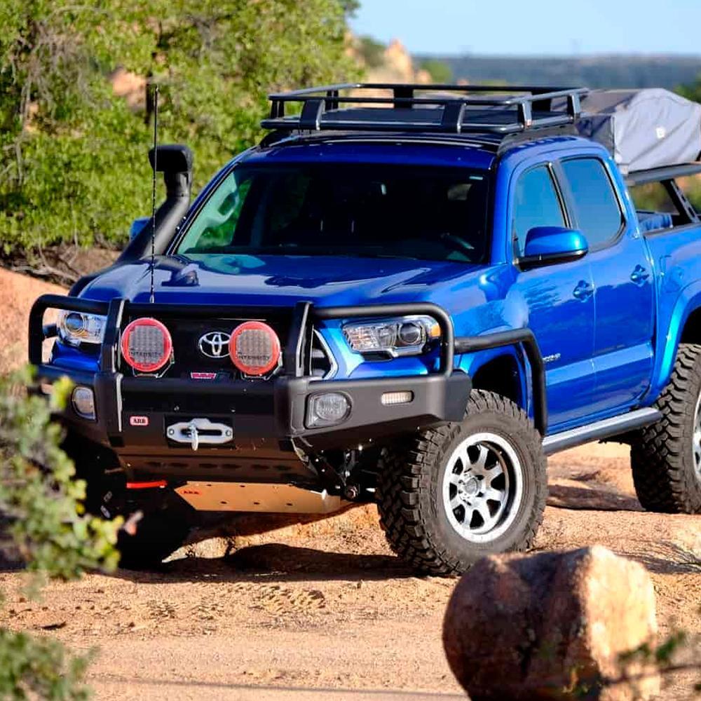 A blue Toyota Tacoma is parked in the desert, offering reliable cargo transportation and equipped with a Steel Roof Rack System for Jeep Wrangler 2018-2020 3813030KJL from ARB for enhanced off-roading capabilities.