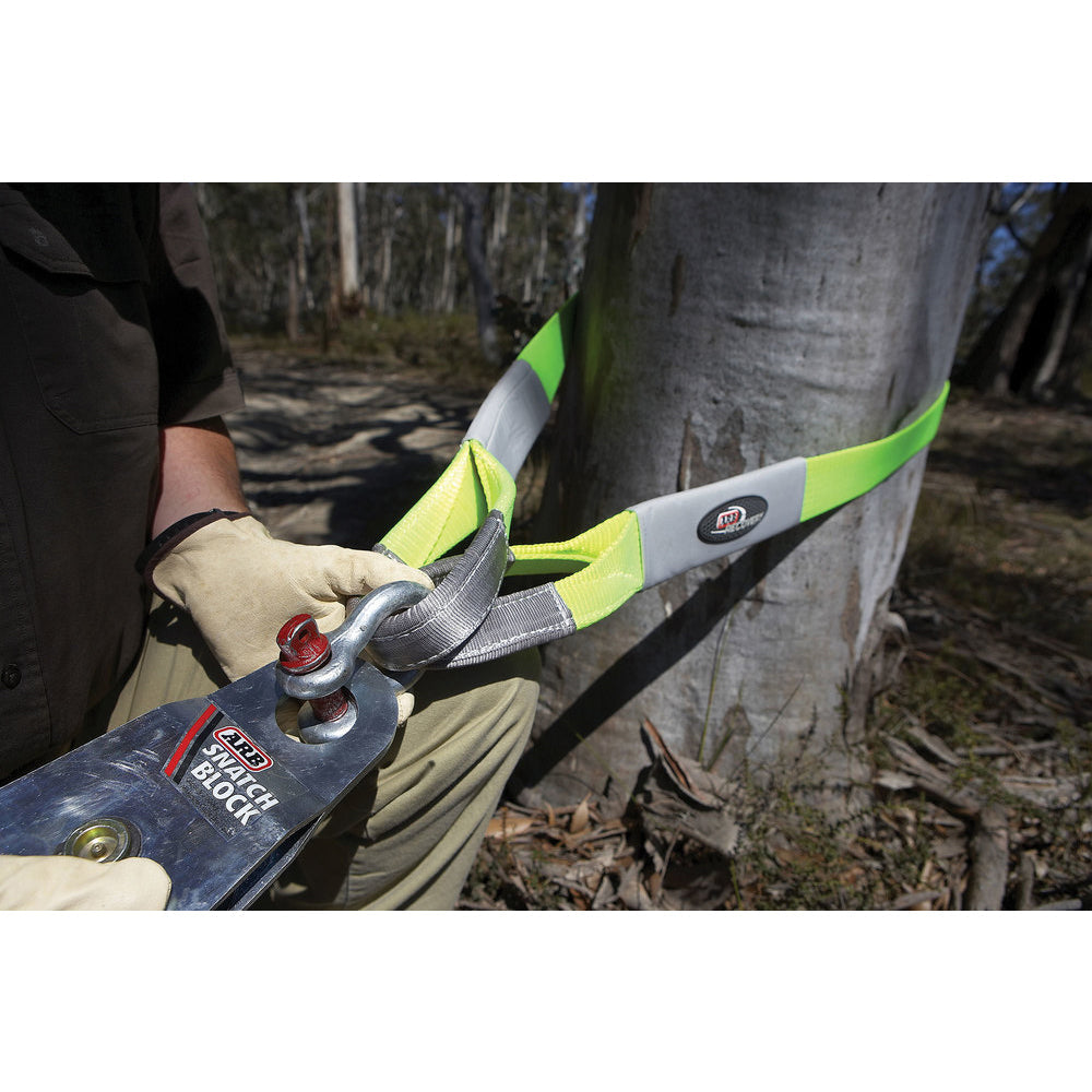 A person is using an ARB chainsaw to cut down a tree while ensuring the safety of their anchor point and using ARB Tree Protectors for protection.