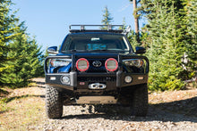 Load image into Gallery viewer, An ARB Summit Winch Front Bumper (Black) 3421570K for Toyota 4Runner (2010-2023) parked on a dirt road, showcasing its robust bumper design and equipped with driving lights.