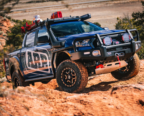A blue 4WD Ford Ranger is driving down a rocky trail, equipped with the ARB Under Vehicle Skid Plates System For Toyota Hilux Revo/Rocco (2015-2022) 5414200.