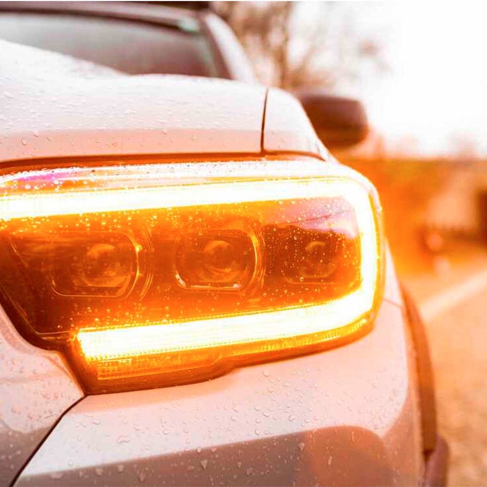 The Morimoto XB LED headlights Amber DRL LF530.2-A-ASM for Toyota Tacoma (2016 - 2022) illuminate the rainy road ahead.