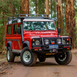 A red Land Rover parked on a dirt road, showcasing its impressive ground clearance and equipped with the OME 2 inch Lift Kit for Land Rover Defender 110 (85-17) from Old Man Emu.