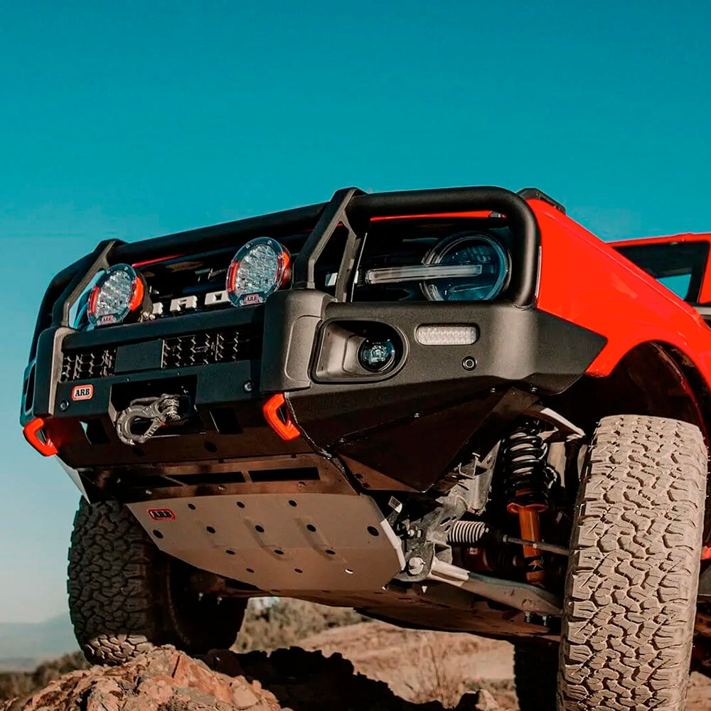 A red Nissan Bronco, equipped with Old Man Emu Front Coil Springs 3200 for Ford Bronco Black Diamond, Badlands (2021-ON) from ARB, is parked on a rock. Its ride height increases significantly due to the easy installation of these upgraded components.