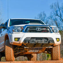 Load image into Gallery viewer, A white Toyota Tacoma is driving down a dirt road with the ARB Old Man Emu Front Nitrocharger Sport Strut 90010 for Toyota 4Runner/ FJ Cruiser / Prado 150 Series from Old Man Emu.