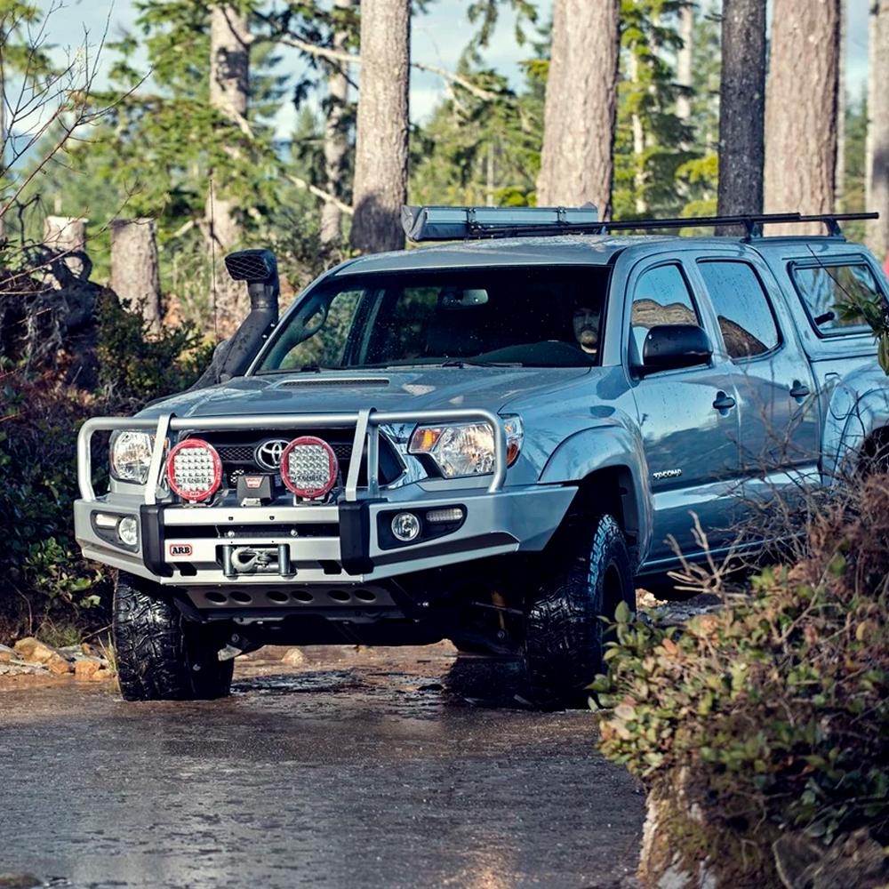 A blue Toyota Tacoma, with easy installation of Old Man Emu Front Coil Springs 2886 for Toyota Tacoma/ Tacoma V6 - 1.5 inch Estimated Lift by ARB, is driving through the woods effortlessly as its ride height increases.
