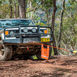 An ARB Snatch Block 7000 - 30,000lb Breaking Strength ARB2091A with a rope attached to it is parked in the woods, ready to tackle the carrying capacity needed for an adventurous trip. Equipped with roof racks, this vehicle ensures optimal SEO keywords like ARB.