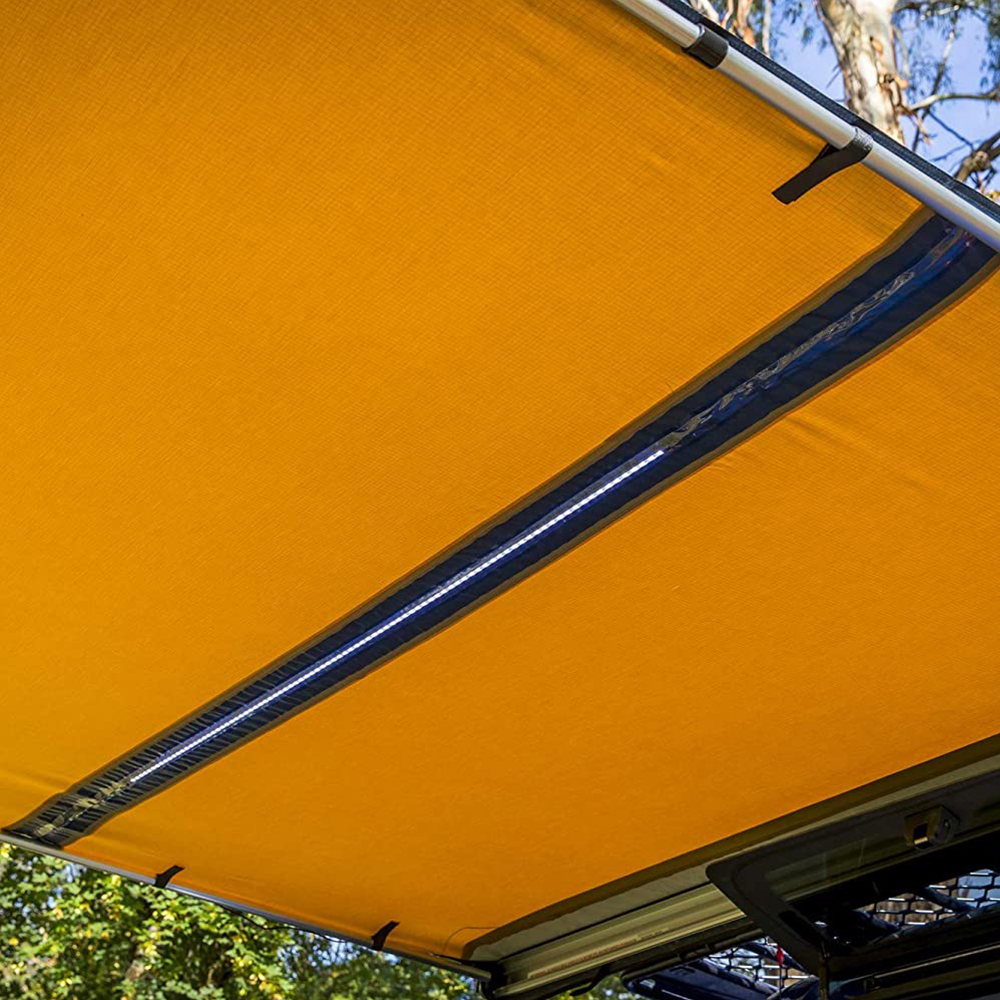 A retractable yellow ARB Touring Awning with Light 814409, designed to be waterproof, hanging from the roof of a jeep equipped with roof racks.