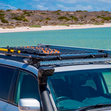 Load image into Gallery viewer, An ARB jeep with an Alloy Flat Rack With Mesh Floor for Toyota Land Cruiser 200 Series ARB 4900040MKLC2 on top of it near the ocean, providing maximum protection and equipped with an airbag compatible system.