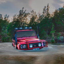 Load image into Gallery viewer, A robust red Old Man Emu Land Rover effortlessly maneuvers through a watery terrain, showcasing its exceptional ground clearance with the OME 2 inch Lift Kit for Land Rover Defender 110 (85-17).