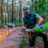 A man wearing ARB Winching Gloves, kneeling in the mud with a green tool.