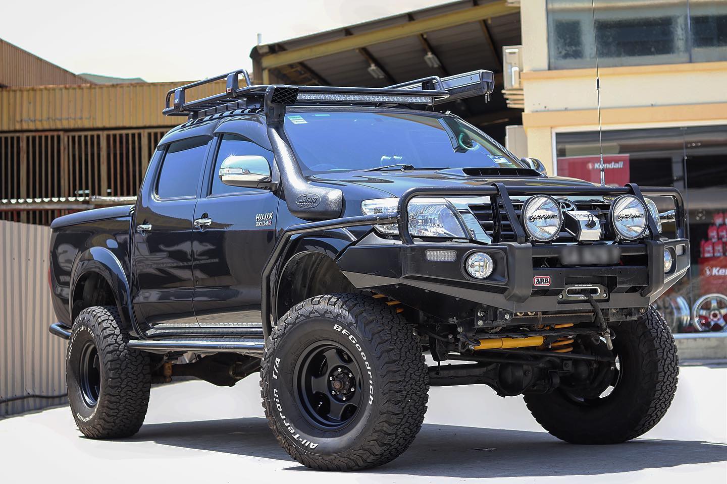 A black Old Man Emu Toyota Hilux parked in front of a building.