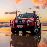 A red Toyota Hilux with ARB Old Man Emu Rear Coil Springs 2896 for Prado150 Series, FJ Cruiser, 4Runner - Constant Load 440 lbs., providing excellent ride height, parked on the beach at sunset. Experience easy installation with this stunning vehicle.