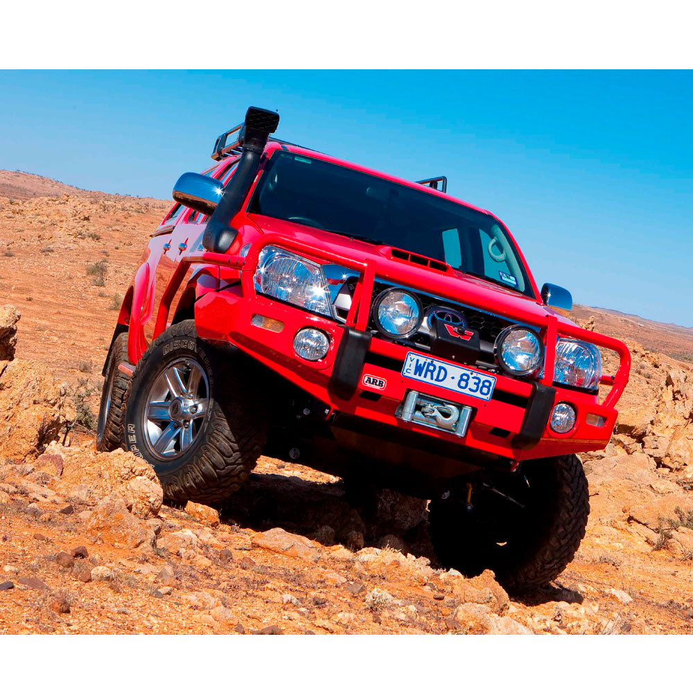 A red Toyota Tacoma with Old Man Emu BP-51 suspension and shock absorbers is driving through a desert.