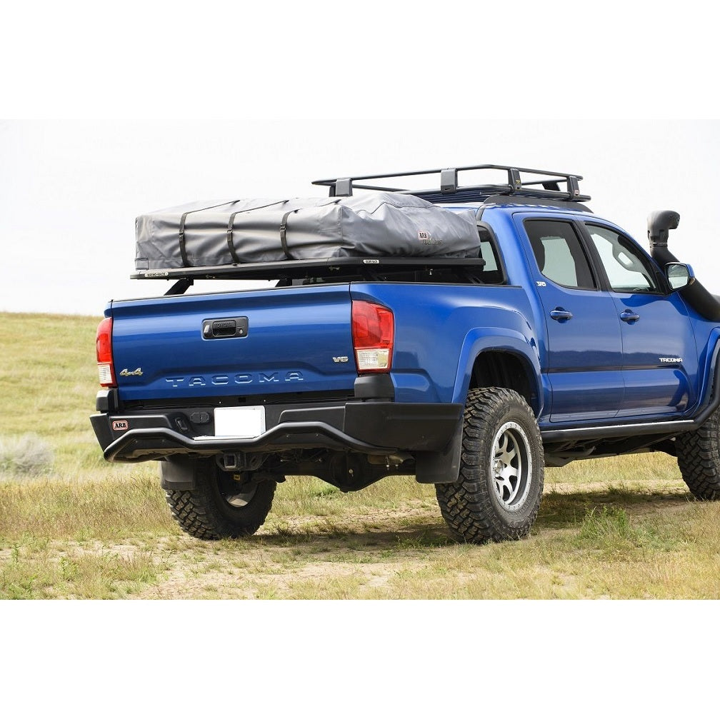 A blue Toyota Tacoma with a roof rack on it, equipped with the ARB Summit Rear Bumper 3623040 For Toyota Tacoma 2016-2023 and a tow hitch.