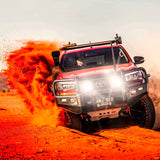 An intense red ARB Tacoma driving through the dimming desert.
