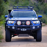 A blue Toyota Tacoma, equipped with an ARB Steel Flat Rack Kit 52” x 44” for Toyota FJ Cruiser 2007-2014 ARB 3800250KF, is driving down a dirt road.