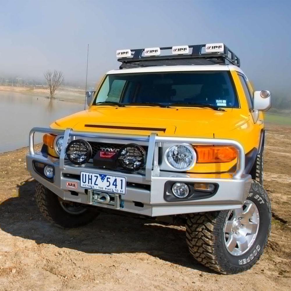 A yellow Toyota FJ Cruiser with the Roof Rack Components Toyota FJ Cruiser 2007-2014 ARB 3720110 roof racks and a high capacity mounting system parked next to a body of water.
