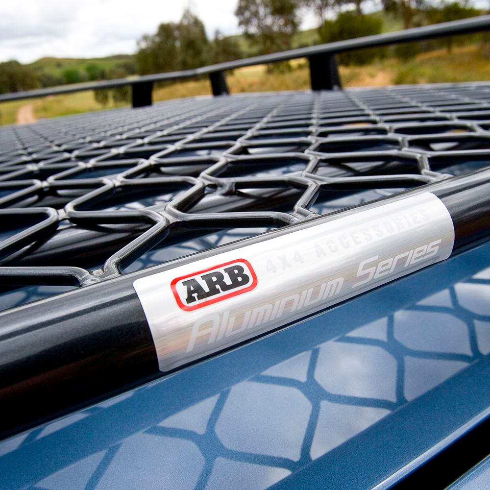 A blue car with an ARB Steel Basket Rack With Mesh Floor 87” X 44” attached to it for Toyota Land Cruiser 200 Series 2008 - 2020.
