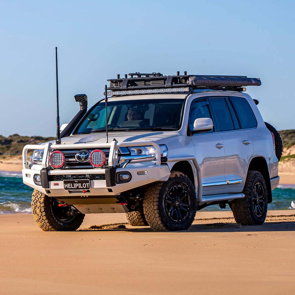 A white ARB Alloy Flat Rack With Mesh 87”X 44” for Toyota Land Cruiser 200 Series 2008 - 2020, known for its steel construction and maximum protection, parked on the beach.