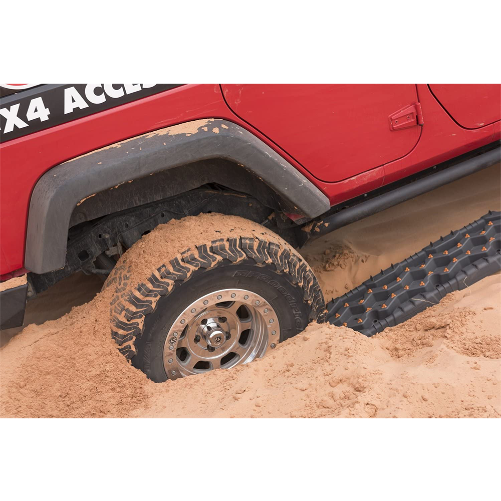 A Jeep Wrangler, a four-wheel drive vehicle, is stuck in the sand and requires the assistance of TRED Pro Recovery Device TREDPROBB - Black, an off-road recovery device by ARB.