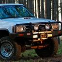 A white ARB Deluxe Bull Bar 3414090 for Toyota Land Cruiser parked in a wooded area, providing maximum protection with its steel construction.