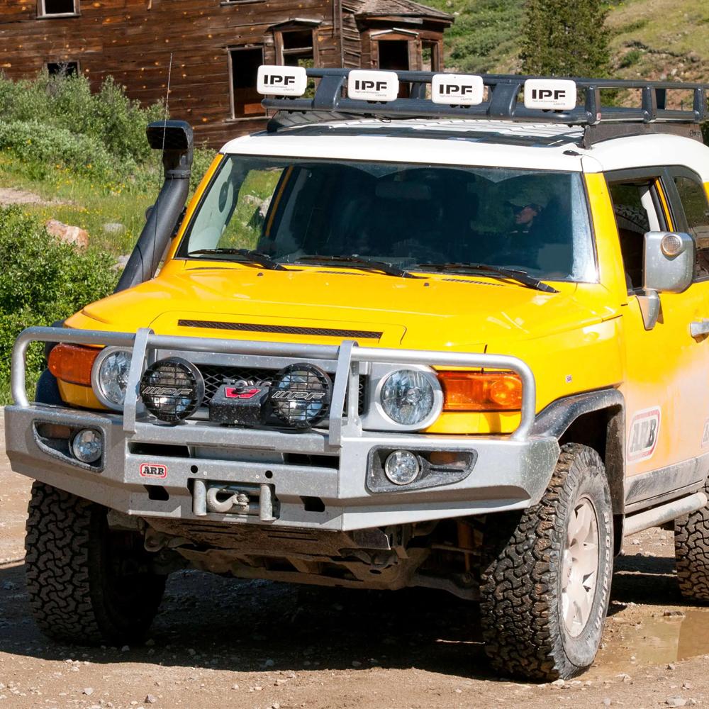 A yellow Toyota FJ Cruiser equipped with ARB Roof Rack Components Toyota FJ Cruiser 2007-2014 ARB 3720110, featuring a high capacity mounting system, driving down a dirt road.