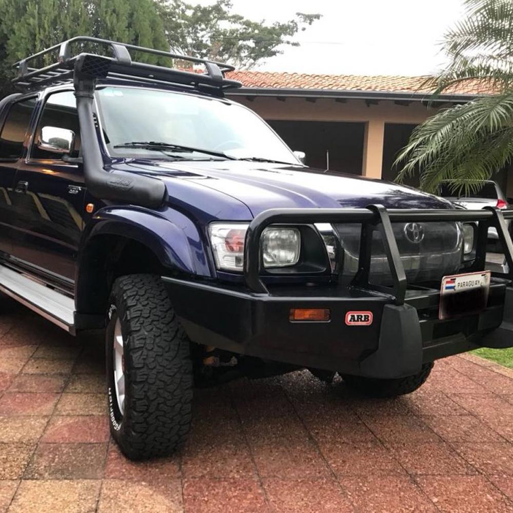 A blue Toyota Tacoma, fitted with a Roof Rack Fitting Kit for Toyota Hilux DCab 1997-2011 ARB 3714010 from the brand ARB, parked on a driveway, offering secure storage and high capacity.