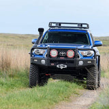 A blue ARB Toyota Tacoma with high capacity is driving down a dirt road.