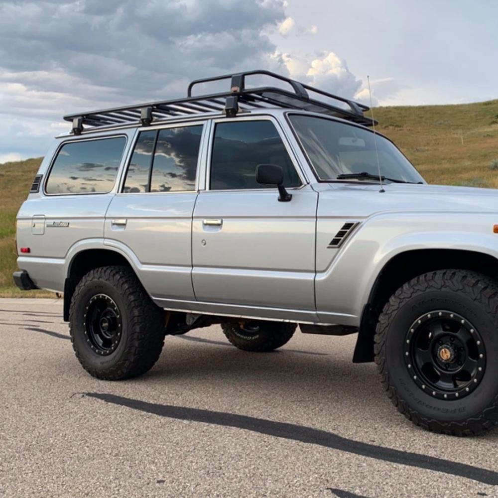 A silver Toyota Land Cruiser parked on the side of the road equipped with ARB Touring Roof Racks 3813200KJK for increased carrying capacity.