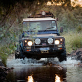 An OME 2 inch Lift Kit-equipped Land Rover Defender 110 (85-17) effortlessly traversing a riverbed, showcasing Old Man Emu's exceptional suspension system and impressive ground clearance.